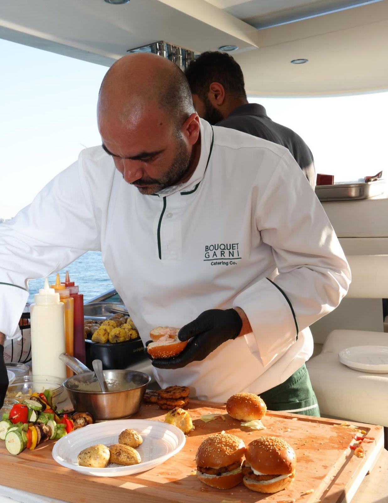 Private chef preparing gourmet burgers and grilled appetizers aboard a luxury yacht in Marina Dbayeh, Lebanon, during a summer celebration.